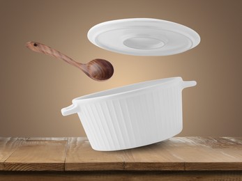 Image of Saucepan, wooden ladle and lid in air on pale brown background