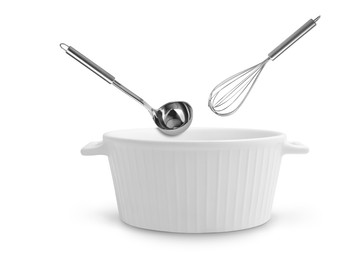 Ladle and whisk in air over saucepan on white background