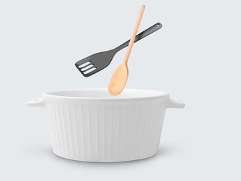 Image of Slotted spatula and wooden spoon in air over saucepan on white background