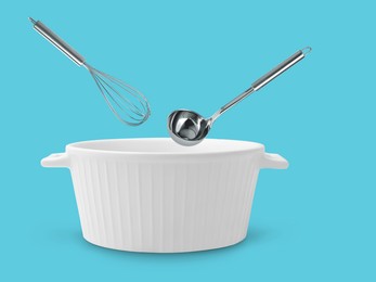 Ladle and whisk in air over saucepan on light blue background