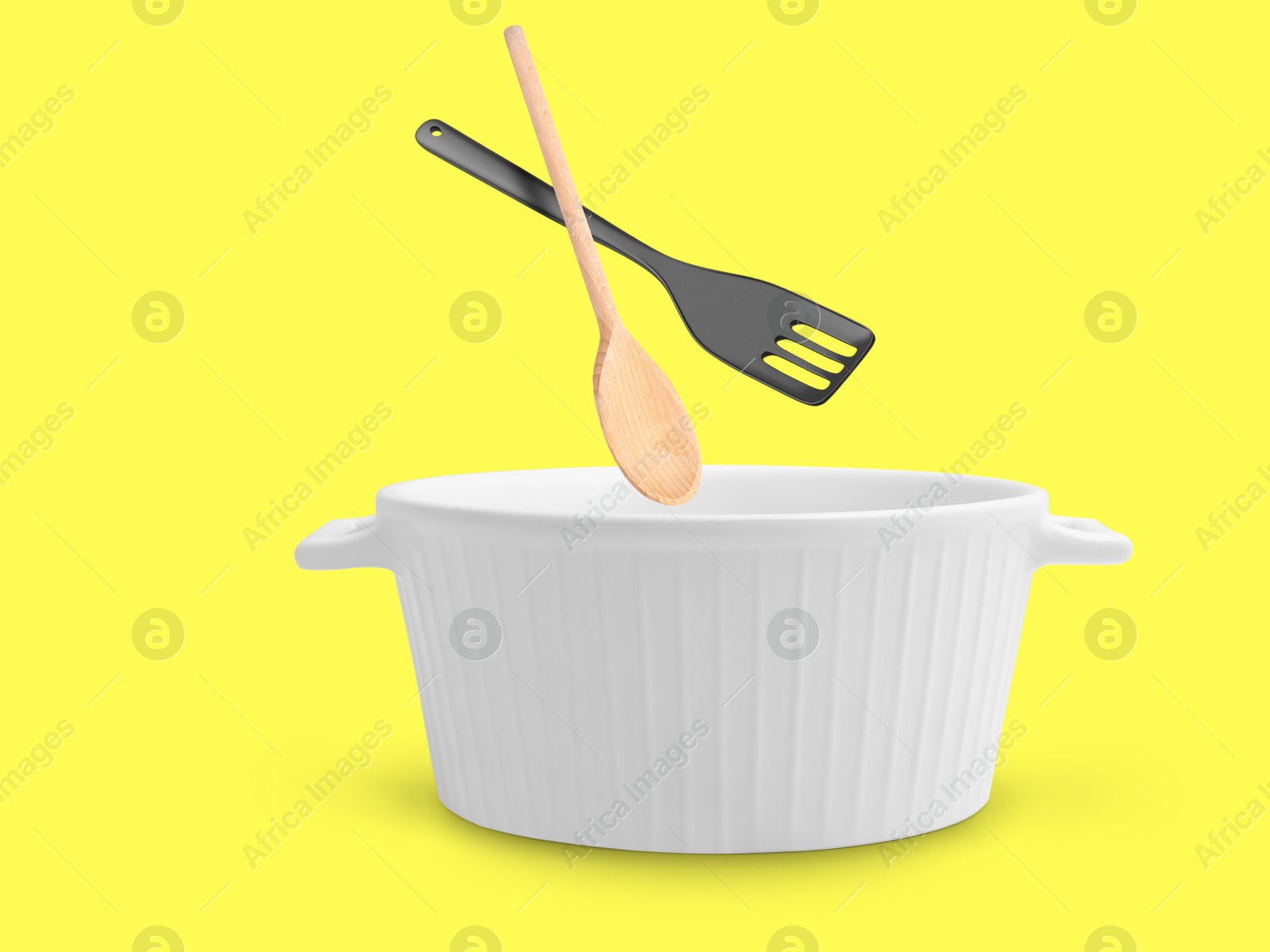 Image of Slotted spatula and wooden spoon in air over saucepan on yellow background