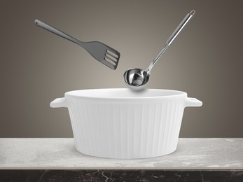 Slotted spatula and ladle in air over saucepan on table against grey background