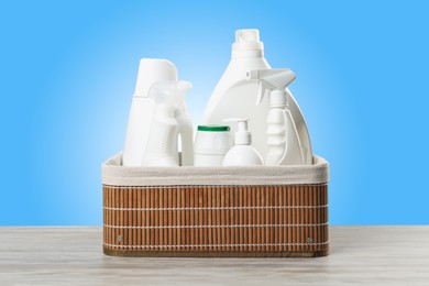 Image of Eco-friendly cleaning products in basket on wooden table against light blue gradient background