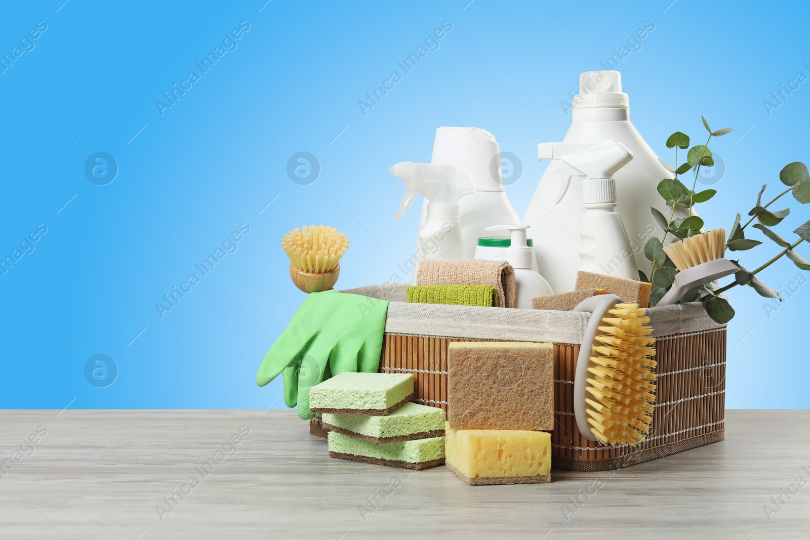 Image of Eco-friendly cleaning products and eucalyptus branches on wooden table against light blue gradient background, space for text