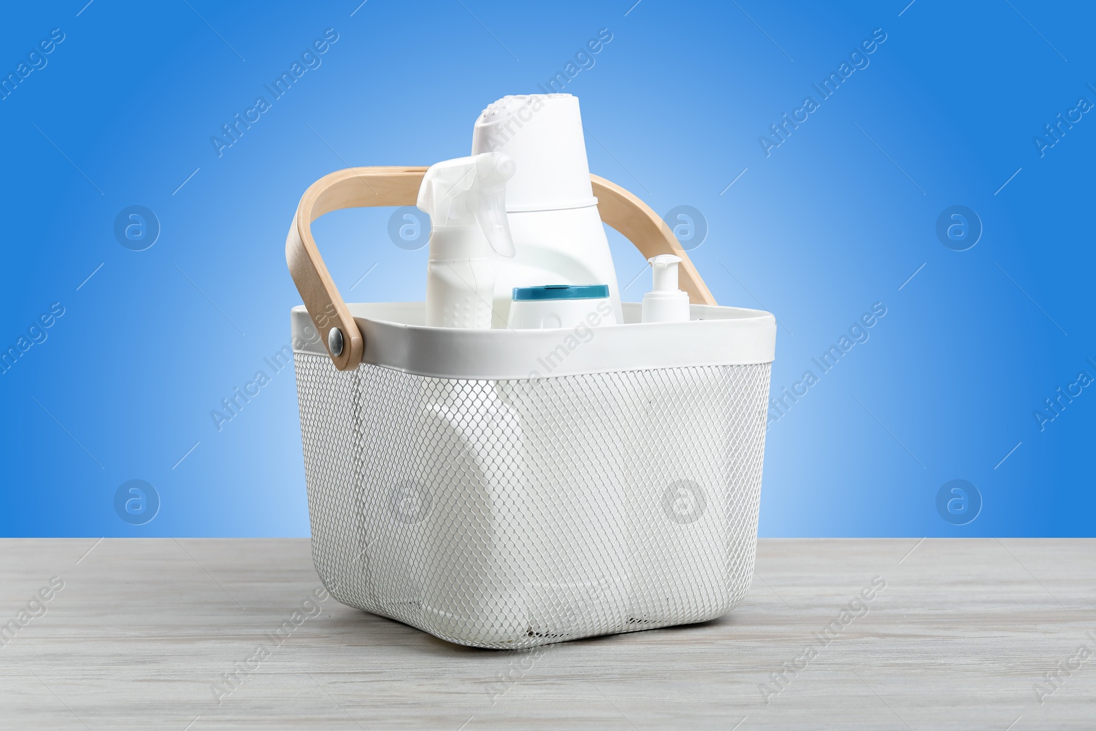 Image of Eco-friendly cleaning products in basket on wooden table against light blue gradient background