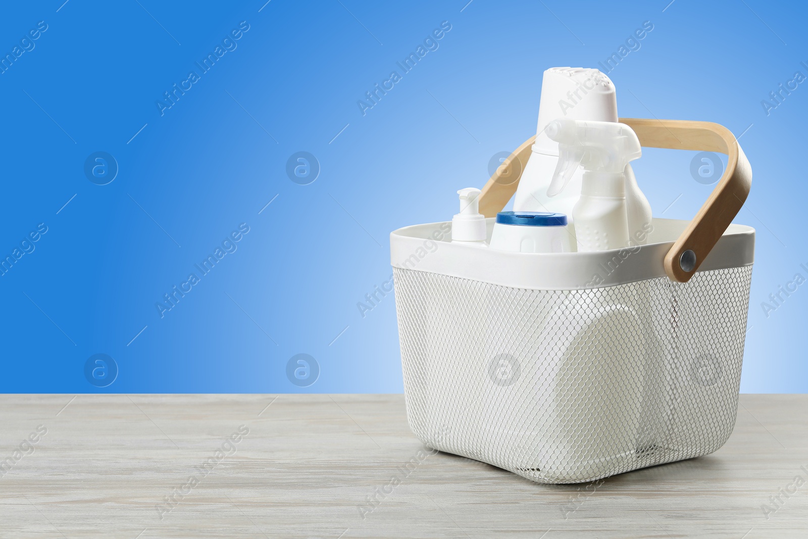 Image of Eco-friendly cleaning products in basket on wooden table against light blue gradient background, space for text