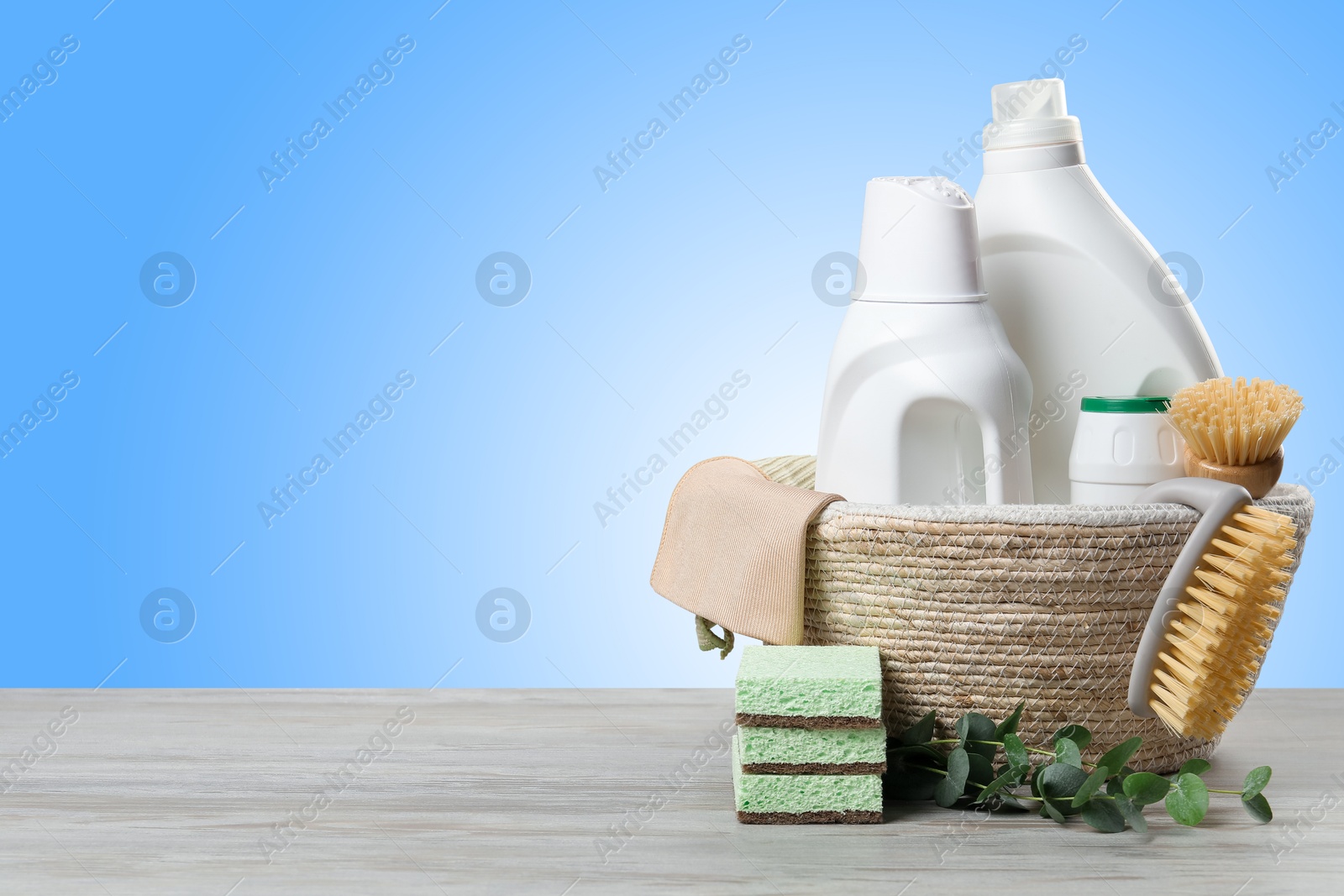 Image of Eco-friendly cleaning products and green branches on wooden table against light blue gradient background, space for text