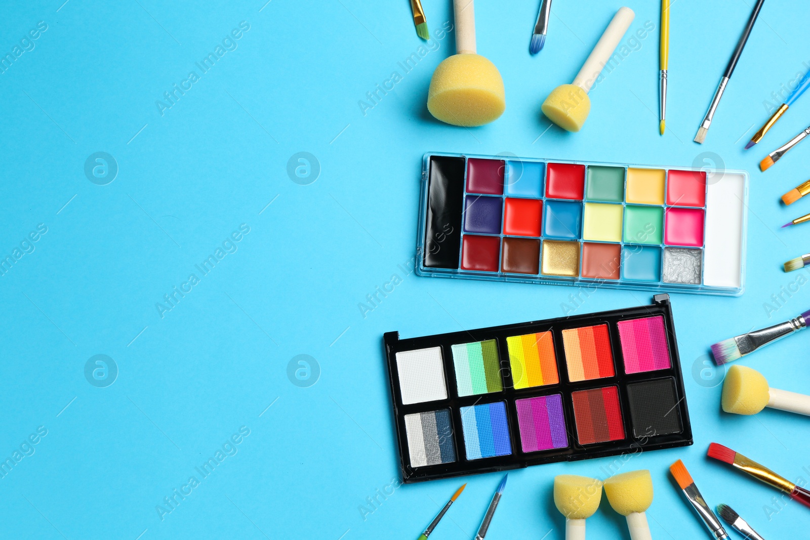 Photo of Bright face paints, brushes and sponges on light blue background, flat lay. Space for text