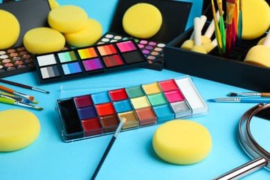 Photo of Bright face paints, brushes, mirror and sponges on light blue background