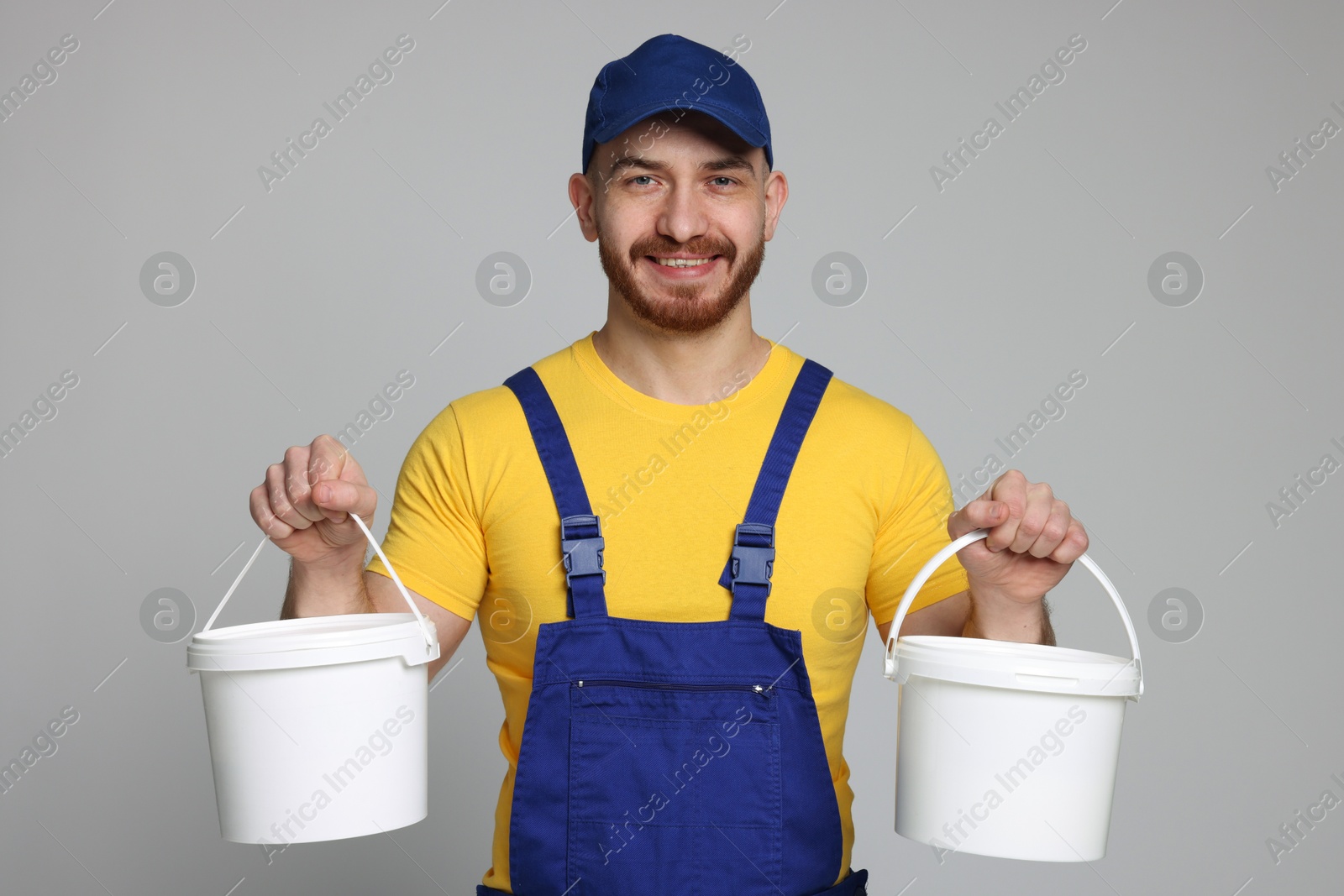 Photo of Professional painter with buckets of paint on light grey background