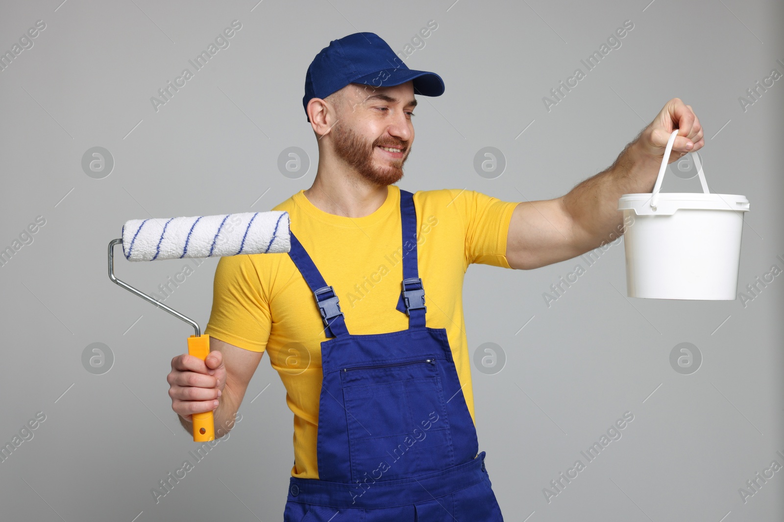 Photo of Professional painter with roller and bucket of paint on light grey background