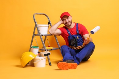 Professional painter with tools and supplies on orange background