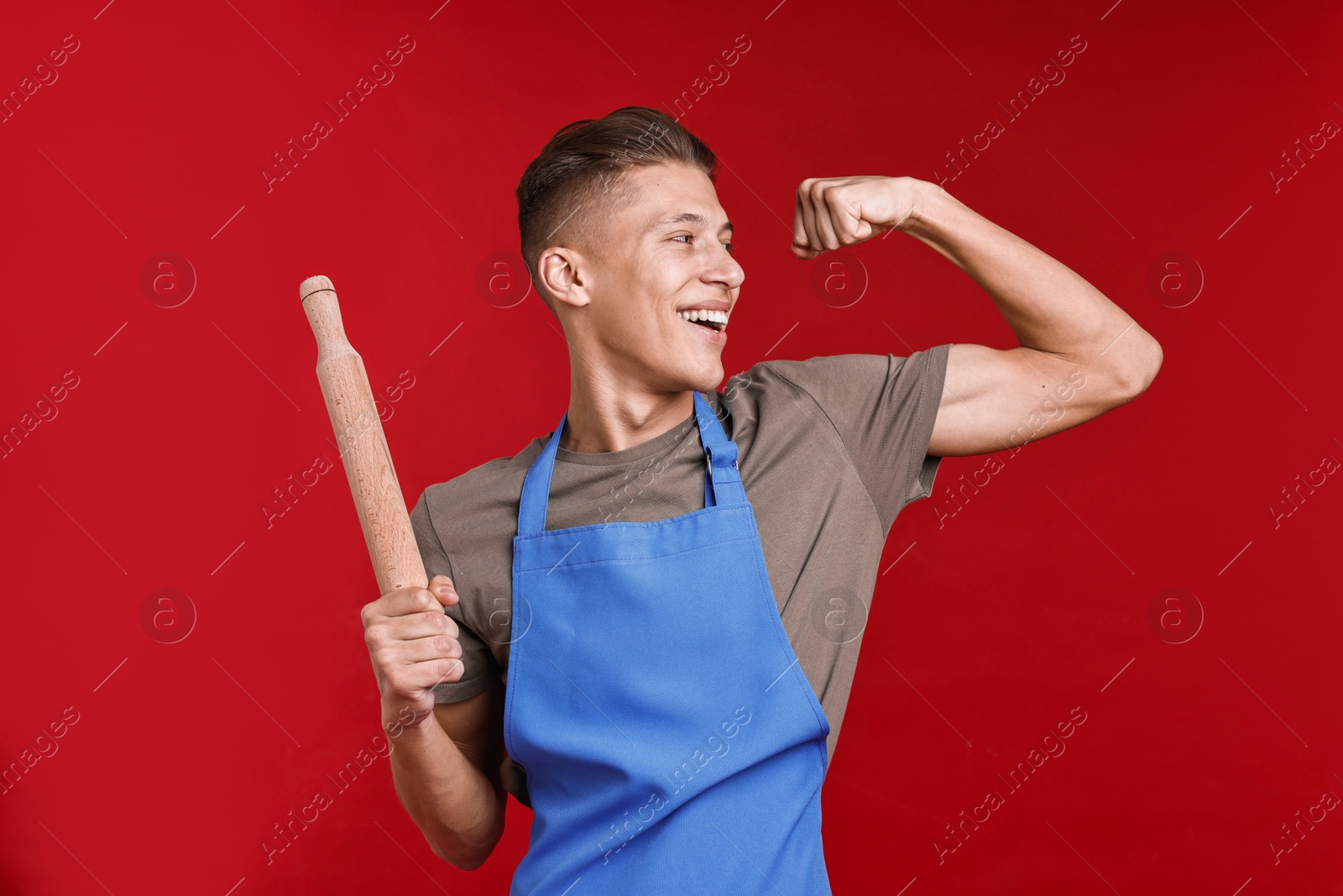 Photo of Happy man with rolling pin showing strength on red background