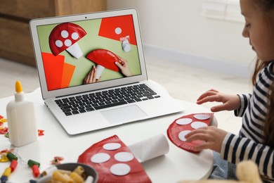 Photo of Little girl making handmade fly agaric by following craft tutorial video at home. Child creativity