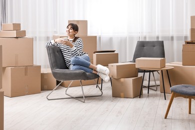 Photo of Moving day. Happy woman with cup of drink and cardboard boxes in new home