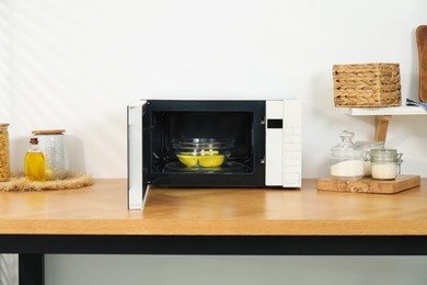 Photo of Open microwave oven with bowl of water and lemons on wooden table indoors