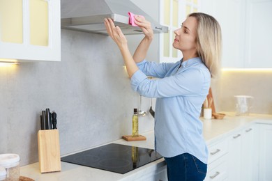 Photo of Woman cleaning kitchen hood with rag indoors