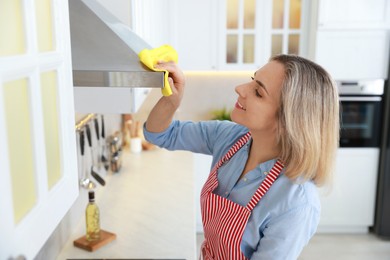 Photo of Woman cleaning kitchen hood with rag indoors