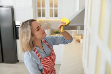 Photo of Woman cleaning kitchen hood with rag indoors