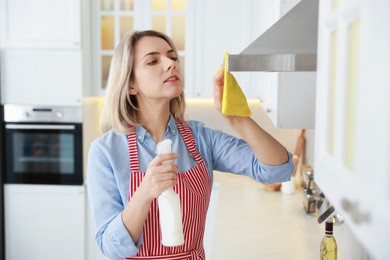 Photo of Woman cleaning kitchen hood with rag and detergent indoors