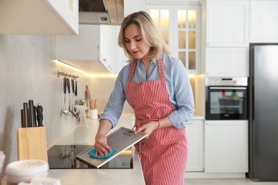 Photo of Woman cleaning filter of kitchen hood with rag indoors