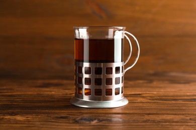 Photo of Glass of aromatic tea in holder on wooden table