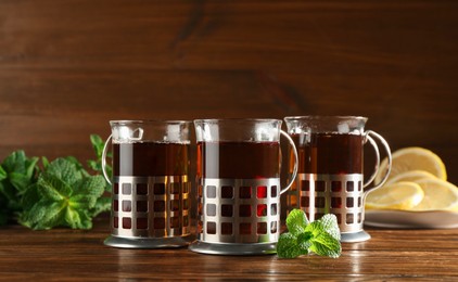 Photo of Glasses of hot tea in holders, mint and lemon on wooden table