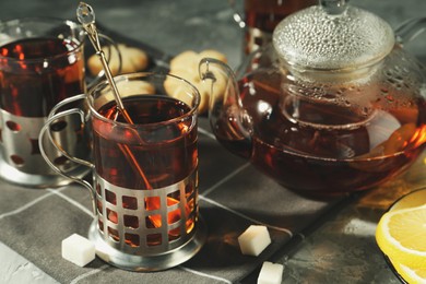 Photo of Glasses of tea in metal holders served on grey table, closeup