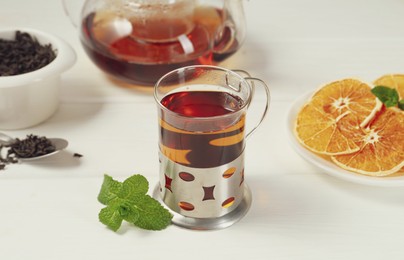 Photo of Glass of tea in metal holder served on white wooden table, closeup