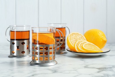 Photo of Glasses of tea in metal holders served on white marble table, closeup