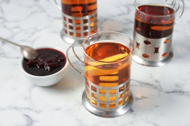 Photo of Glasses of tea in metal holders served on white marble table, closeup