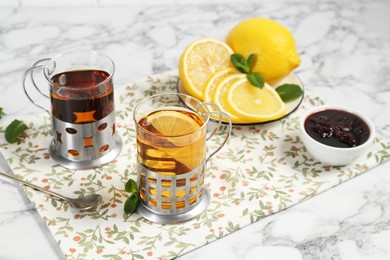 Photo of Glasses of tea in metal holders served on white marble table