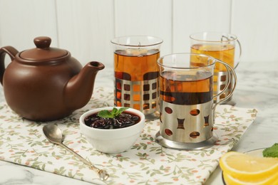 Photo of Glasses of tea in metal holders served on white table, closeup