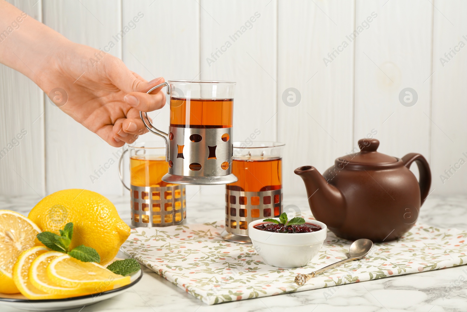 Photo of Woman with glasses of tea in metal holders at white marble table, closeup