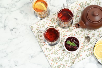 Photo of Glasses of tea in metal holders served on white marble table, flat lay