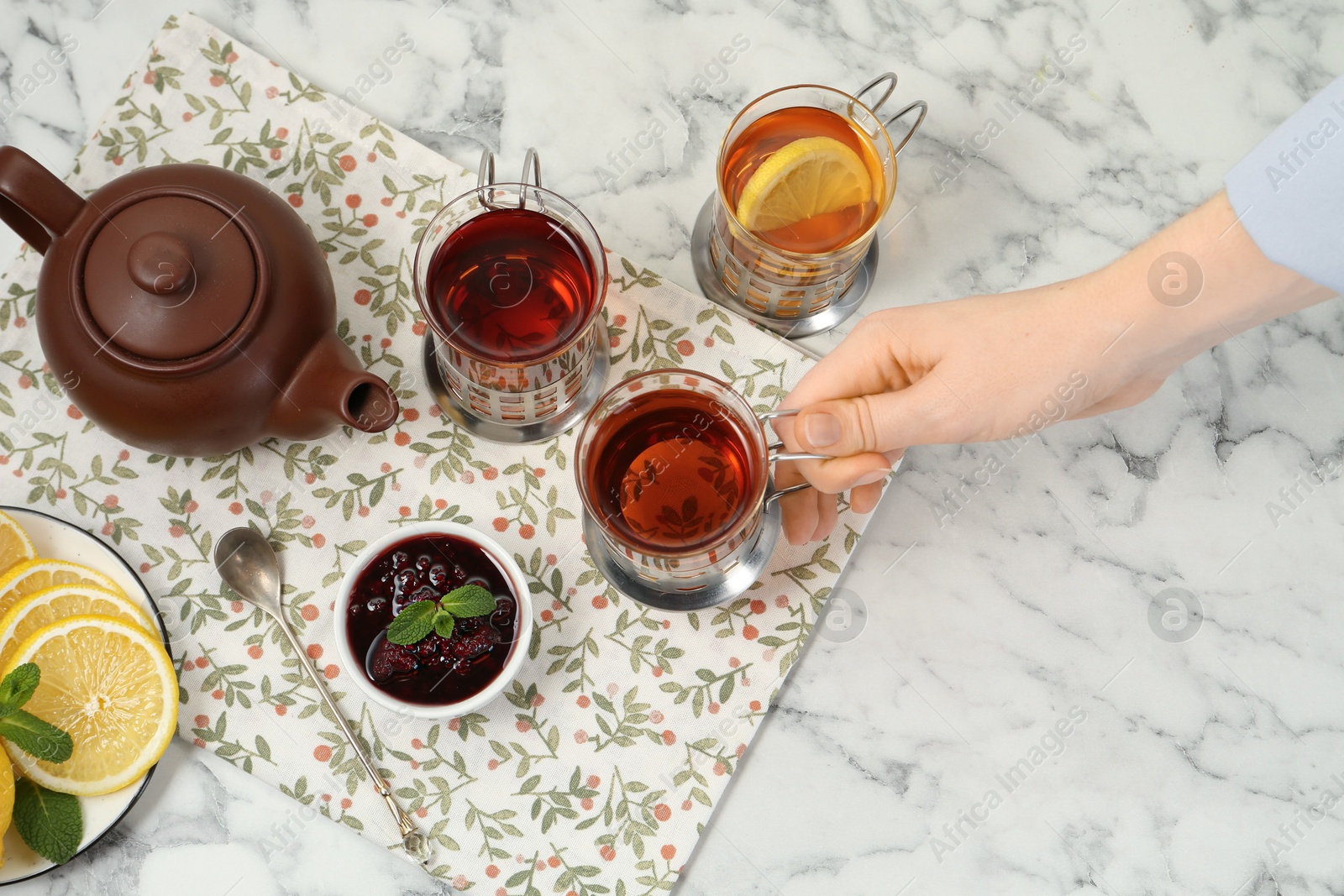 Photo of Woman with glasses of tea in metal holders at white marble table, above view