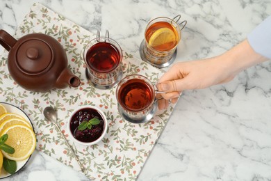 Photo of Woman with glasses of tea in metal holders at white marble table, above view