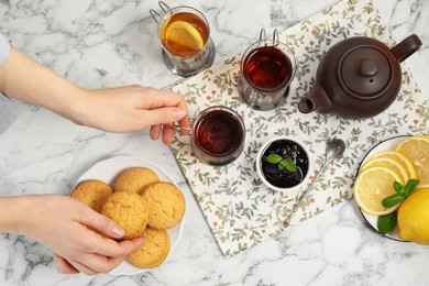 Photo of Woman with glasses of tea in metal holders at white marble table, above view