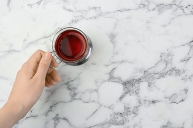 Photo of Woman with glass of tea in metal holder at white marble table, top view. Space for text