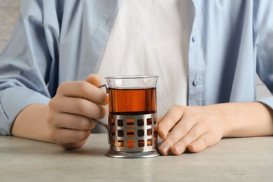 Woman with glass of tea in metal holder at beige table, closeup