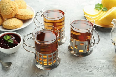 Photo of Glasses of tea in metal holders served on grey textured table, closeup