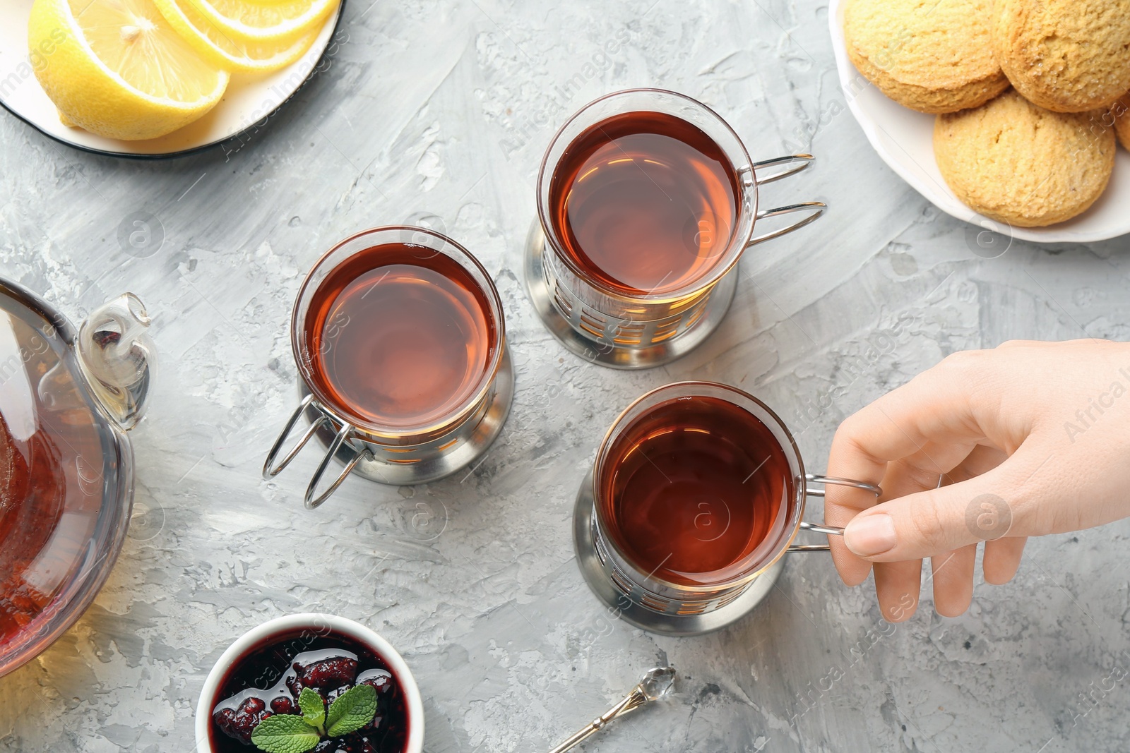 Photo of Woman with glasses of tea in metal holders at grey textured table, top view