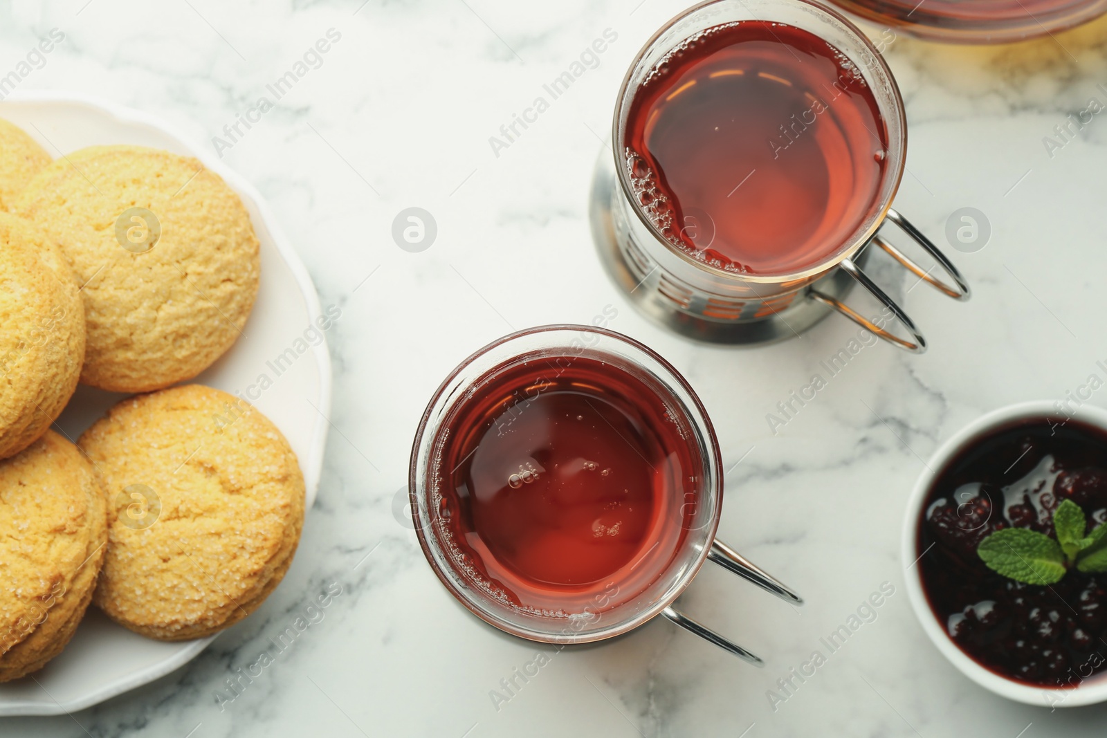 Photo of Glasses of tea in metal holders served on white marble table, flat lay