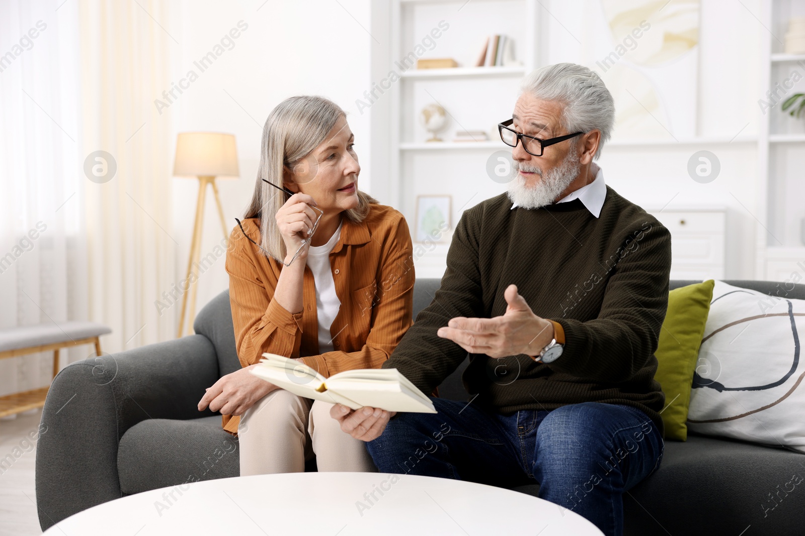 Photo of Cute elderly couple reading book together on sofa at home