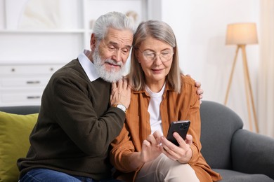 Cute elderly couple with smartphone on sofa at home