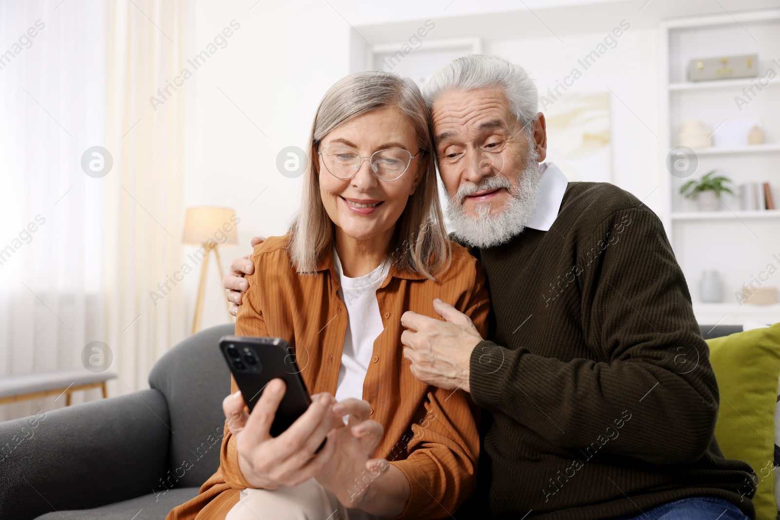 Photo of Happy elderly couple with smartphone on sofa at home