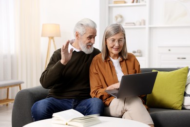 Photo of Happy elderly couple having video call by laptop on sofa at home