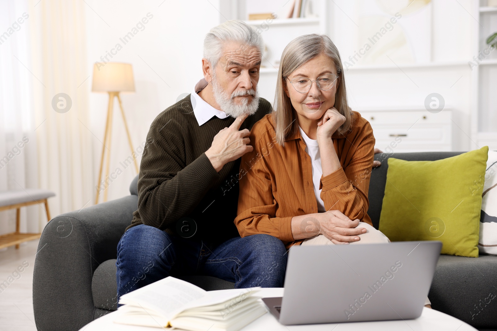 Photo of Cute elderly couple looking at laptop on sofa at home