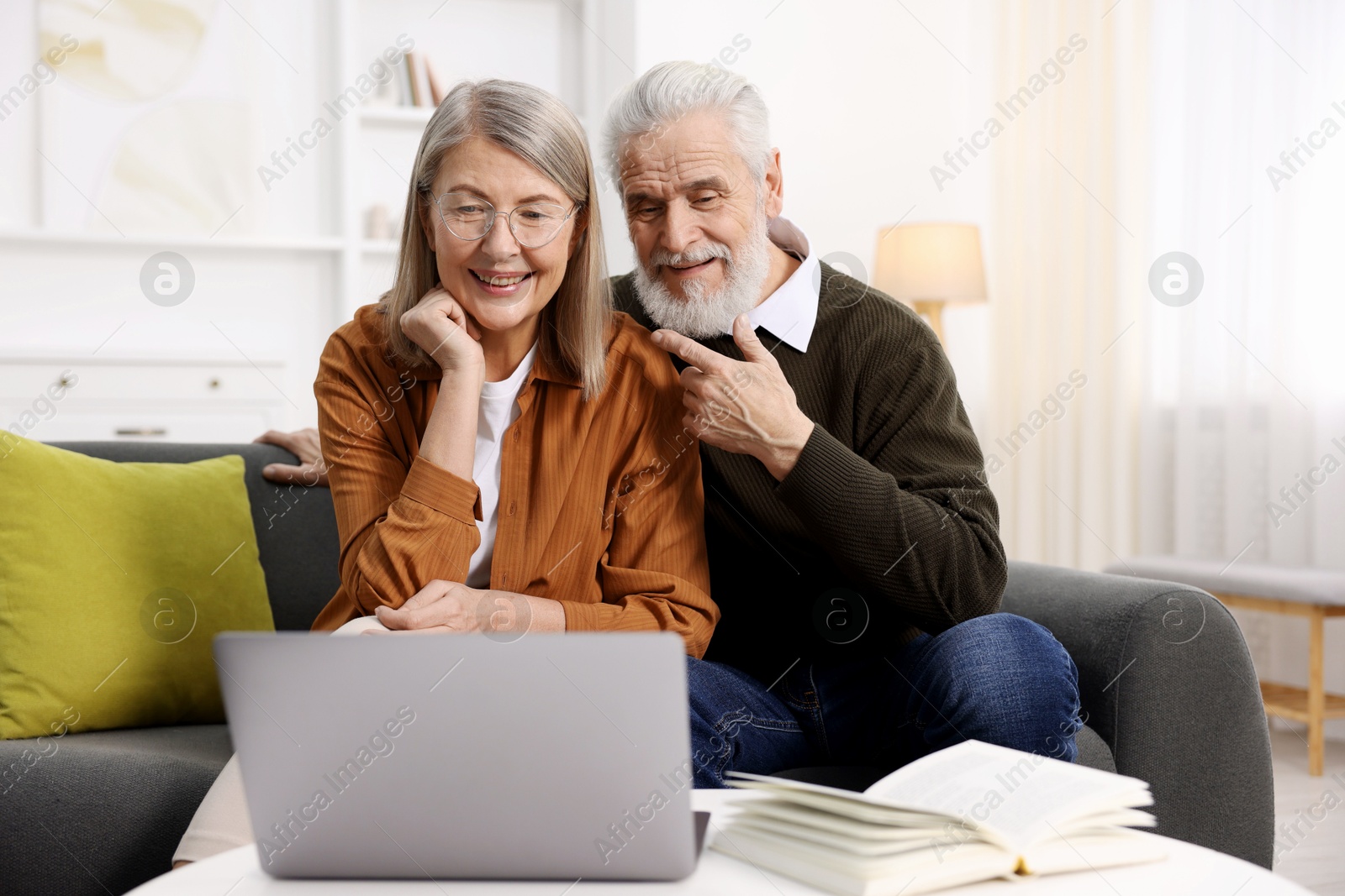 Photo of Happy elderly couple with laptop on sofa at home