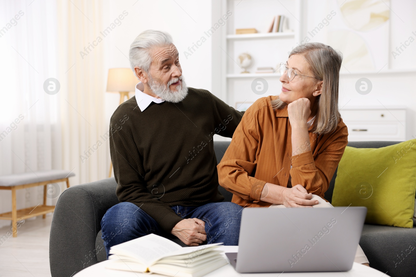 Photo of Cute elderly couple looking at each other on sofa at home